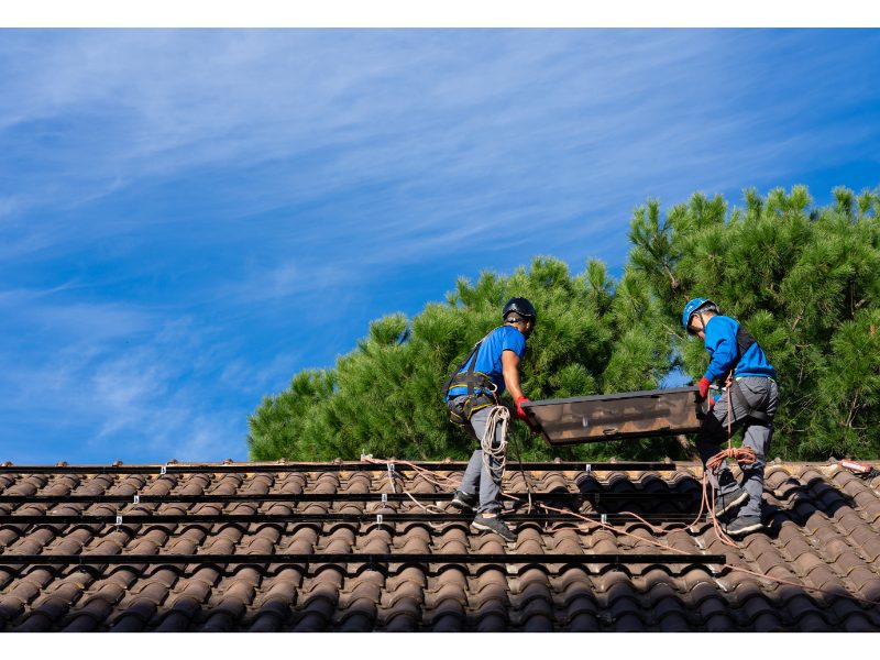 Two roofing workers handling materials on a low-slope roof